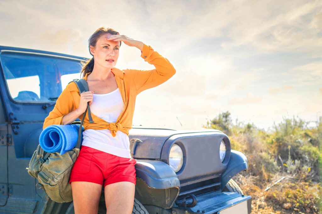 pexels-photo-3779747-3779747 Young woman looking into distance, next to off-road vehicle during summer travel adventure.